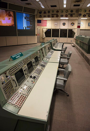 The front row of controllers in Historic Mission Control was referred to as “The Trench” by the flight controllers. Each control station was responsible for a different aspect of a mission. From left to right, the stations are Booster System Engineer, Retrofire Officer, Flight Dynamics Officer and Guidance Officer. Of the hundreds of buttons and controls located at these stations, many have gone missing or have become faded after decades of use. Some of the work stations are even held together by tape.